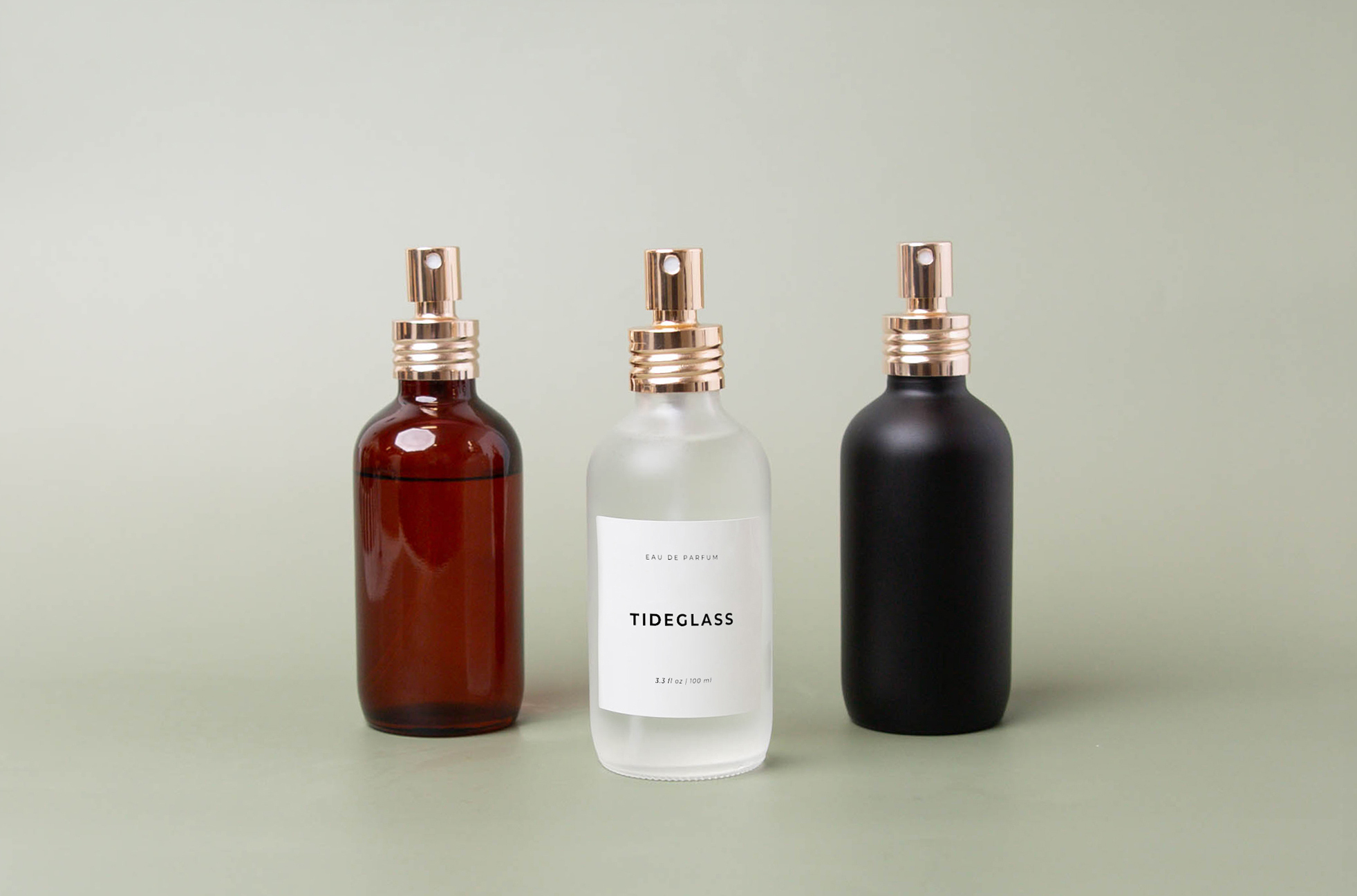 Glass perfume bottles in amber, frosted, and matte black with soft gold pumps.