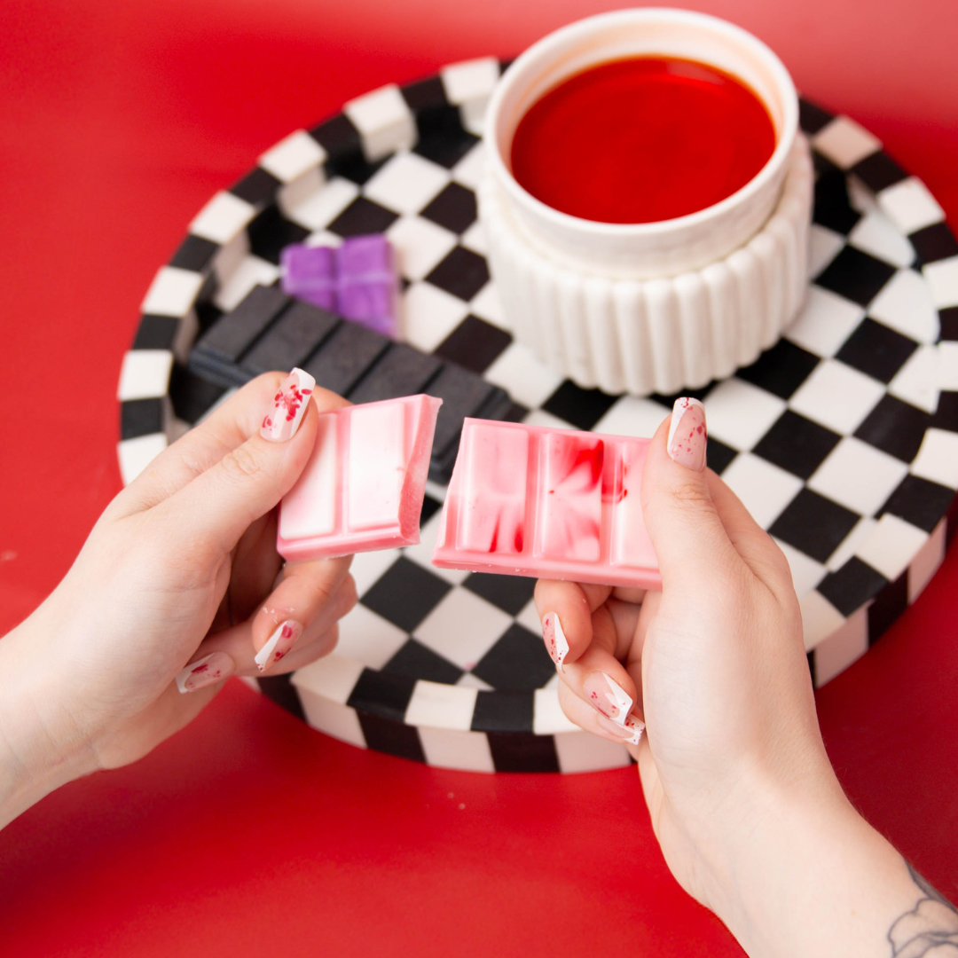 Hand breaking a wax melt bar in front of a wax melter.