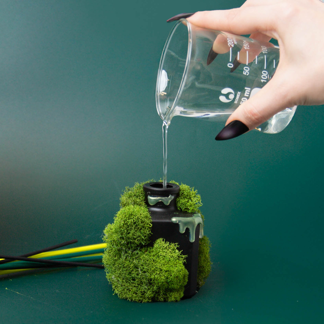 Pouring reed diffuser solution into a matte black cube reed diffuser.