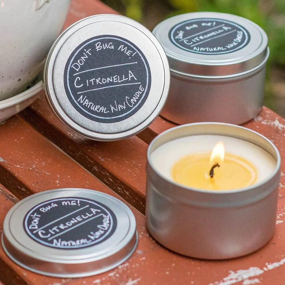 citronella candles in black tins with labels. One candle is burning.