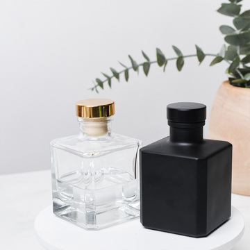 A matte black cube and clear cube reed diffuser bottle on a marble table with eucalyptus in the background.