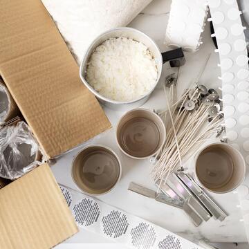 An overhead view of candle supplies like jars, wax, wicks, wick stickers, and wick bars