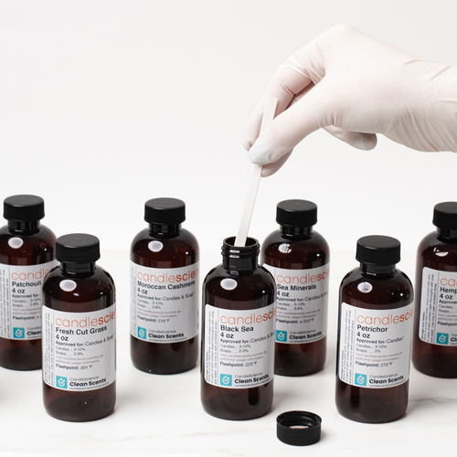 A gloved hand dips a fragrance blotter strip into a bottle of CandleScience fragrance oil