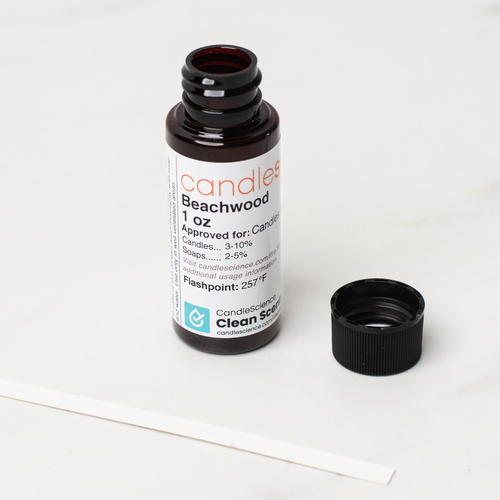 A 1 oz bottle of CandleScience fragrance oil with its lid off and a fragrance blotter strip next to it