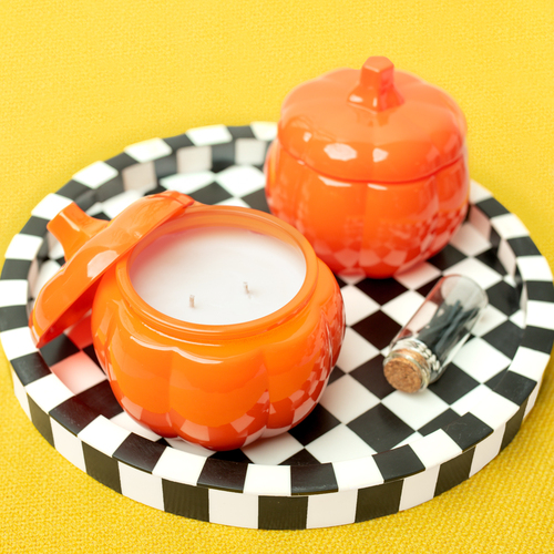 Orange glass pumpkin jars filled with candle wax and wicks. The jars are resting on a black and white checkered table.