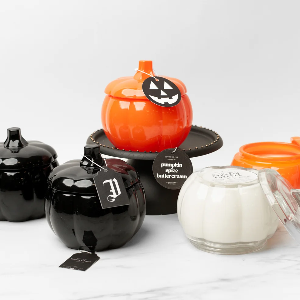 Three glass pumpkin jars in orange, black, and clear on a chess board display stand.