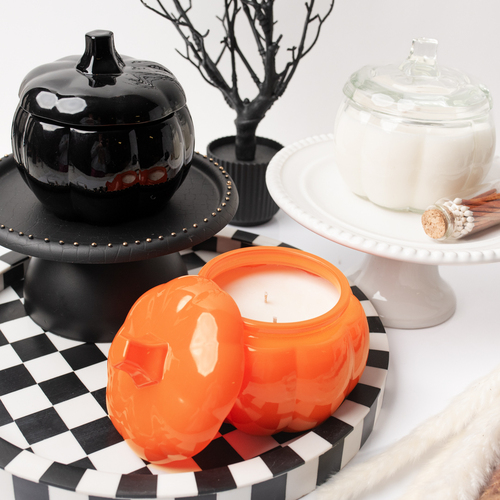 Three glass pumpkin jars in clear, black, and orange on a stylized chess board table. 